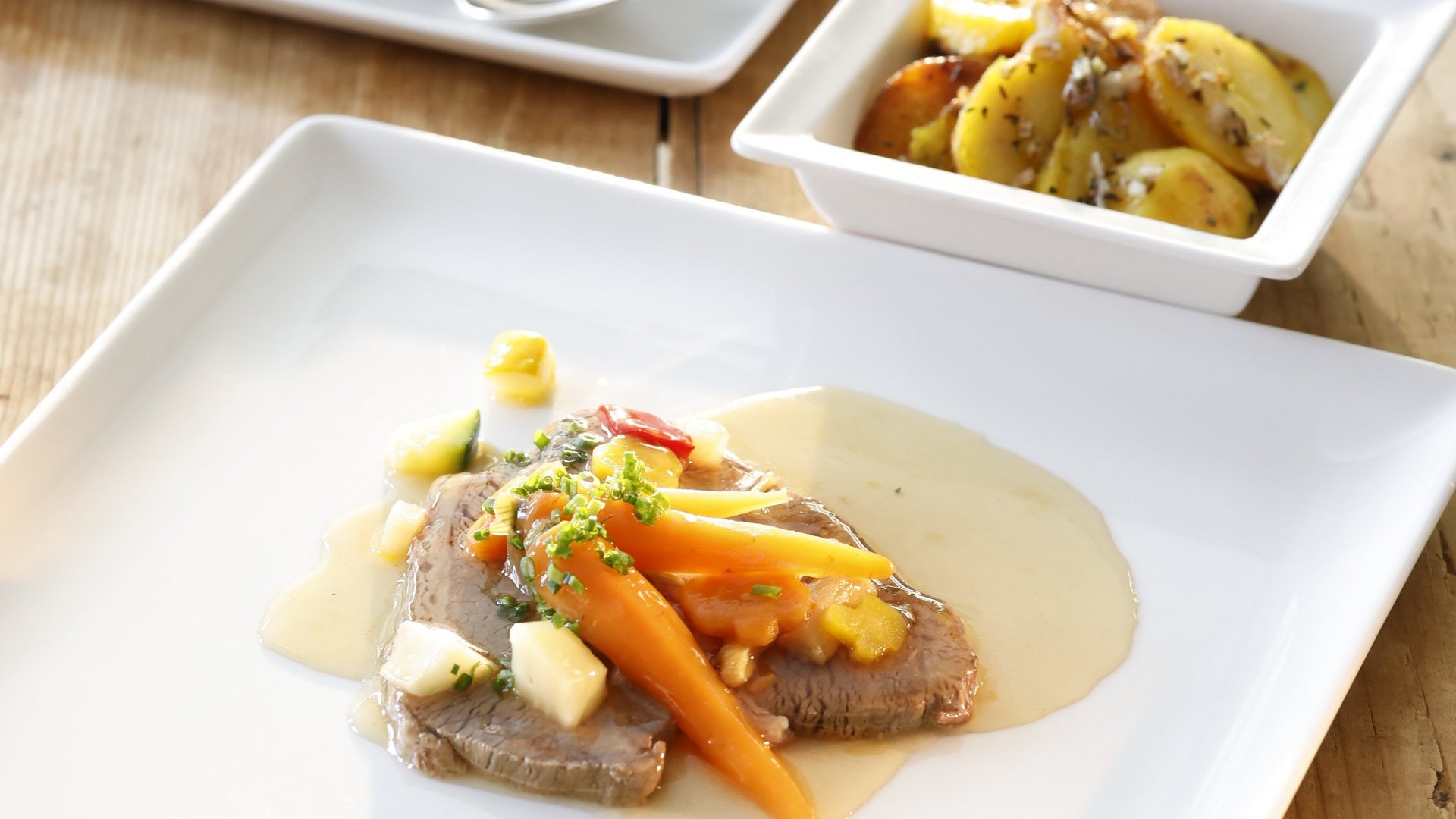 Elegantes Gericht mit zartem Fleisch, buntem Gemüse und Beilagen auf weißen Tellern.