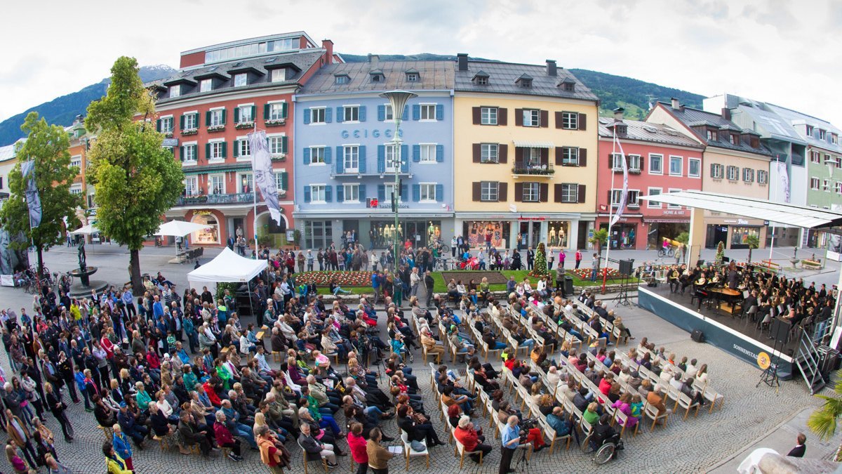 Konzertbesucher vor historischen Fassaden in Lienz, Tirol, mit Bergblick im Hintergrund.