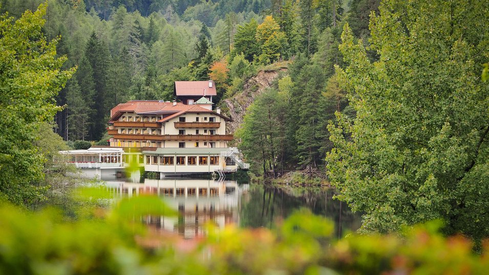 Hotel am ruhigen See, umgeben von grünen Bäumen und sanften Hügeln.