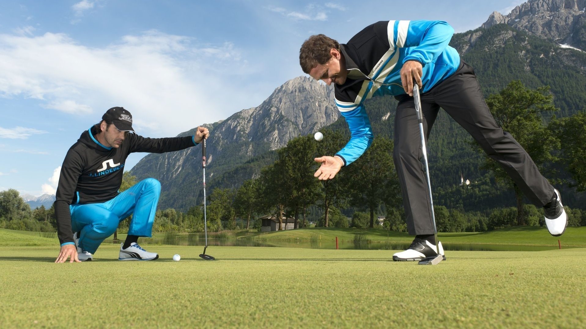Zwei Golfer konzentrieren sich auf dem Grün vor malerischer Bergkulisse.
