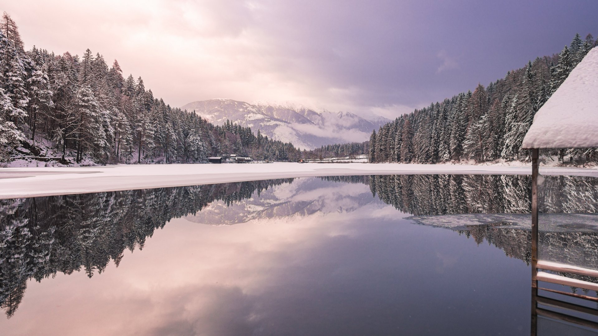 Winterlicher Seezauber Verschneiter See mit reflektierenden Bäumen und Bergen im Hintergrund bei Dämmerung.